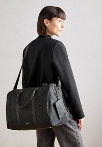 Crna quilted torba s uzorkom ruža, s čvrstim ručkama, odvajanom remenom za rame i držačem za oznaku prtljage. Glatka tekstura.