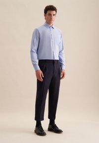 Camicia azzurra chiara con colletto, abbinata a pantaloni blu scuro e scarpe nere stringate. Tessuto morbido, vestibilità su misura.