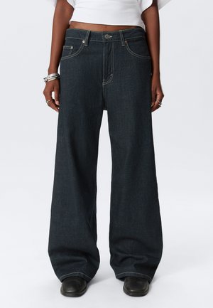 Wide-leg dark denim jeans with yellow stitching, front pockets, and a button-fly closure. The fabric has a smooth texture.