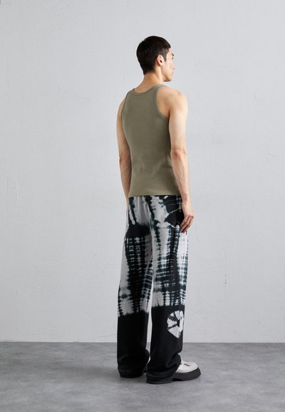 Tricou tip maiou de culoare verde olive, cu un design mulat, asortat cu pantaloni largi alb-negru cu un model tie-dye și inimioare. Pantofi negri, masivi.