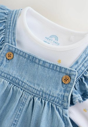 Blauwe denim tuinbroekjurk met gerimpelde mouwen, houten knopen en een wit binnenhemd met een geribbelde structuur en een kleine bloemprint.