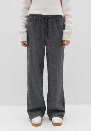 Pantaloni jogger grigi con texture, cintura elasticizzata e coulisse, caratterizzati da un fit rilassato e tasche laterali, abbinati a sneakers bianche.
