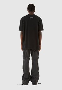 Sort oversized t-shirt med korte ærmer og logodetalje på ryggen, parret med løstsiddende sorte cargo-bukser med sidelommer og smalle mansjetter.