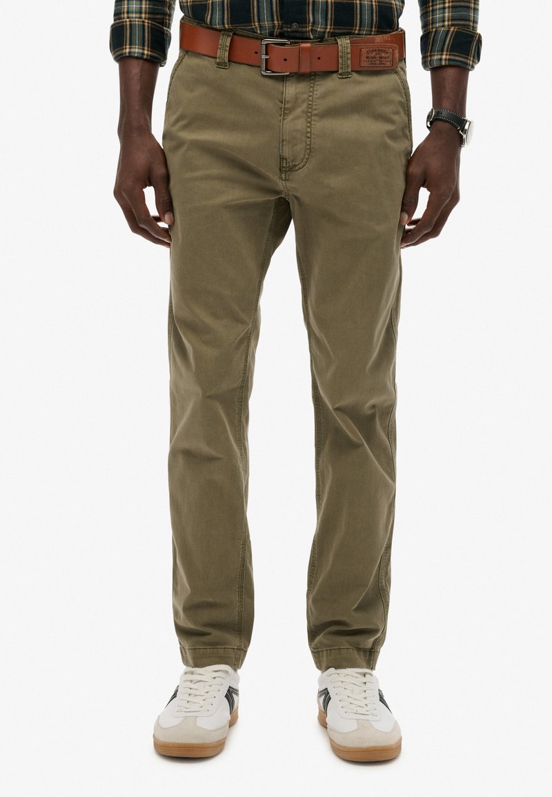 Olijfgroene katoenen chinos met een rechte pijp, voorzien van een brown leren riem en witte sneakers met zwarte accenten.
