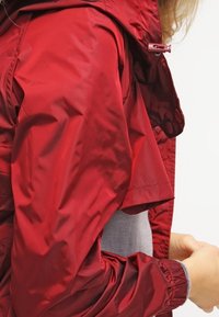 Czerwona wodoodporna kurtka z kapturem, z błyszczącą fakturą, regulowanym ściągaczem i krótkimi rękawami. Gładki materiał i lekk design.