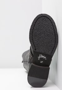 Bottine noire avec tissu texturé, clous métalliques sur le côté et semelle en caoutchouc. Taille 37 indiquée à l'intérieur de la botte.