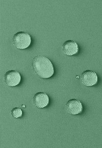 Tessuto verde texturizzato con gocce d'acqua chiare di varie dimensioni che poggiano sulla superficie, evidenziando le proprietà impermeabili del materiale.