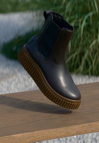 Zwarte leren enkelboot met elastische zijpanelen, textuur bruin rubberen zool en een slank ontwerp. De neus is rond.
