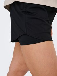 Gros plan d'une personne portant un short de sport noir à double couche avec un ourlet incurvé sur un short intérieur ajusté.