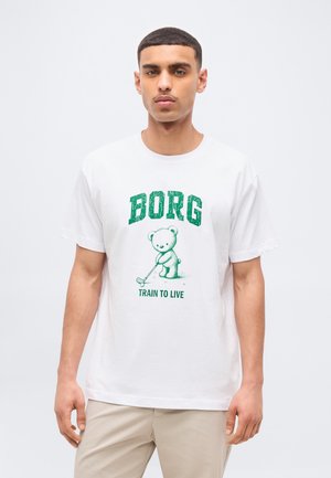 Νέος άνδρας που φοράει λευκό Τ-shirt με πράσινο κείμενο "BORG" και "TRAIN TO LIVE" και ένα καρτούν αρκούδα που παίζει γκολφ.