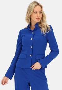 Niebieski żakiet z wysokim kołnierzem, jednolitą zapięciem na guzik, dwoma przednimi kieszeniami i gładką teksturą. Posiada srebrne akcenty okuć.