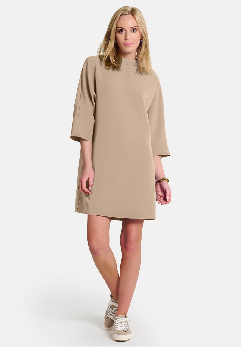 Beige, lyhythihainen mekko, jossa on korkea kaulus ja väljä malli. Yhdistetty beigeihin lenkkareihin. Sileä kangas, jossa on minimimäärä suunnittelutietoja.