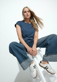 Navyblauwe T-shirt met korte mouwen, losse pasvorm, gecombineerd met ruime lichte spijkerbroek en witte sneakers met zwarte strepen.