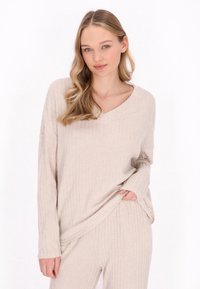 Beige ribbattu loungewear -setti, jossa on pitkähihaiset V-pääntiellä varustettu paita ja siihen sopivat housut. Pehmeä rakenne ja rento istuvuus. Huomaamaton ommelkoristelu.