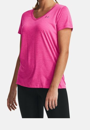 Vrouw draagt een felroze V-hals T-shirt met korte mouwen en een klein logo op de borst, gecombineerd met een zwarte broek tegen een effen achtergrond.