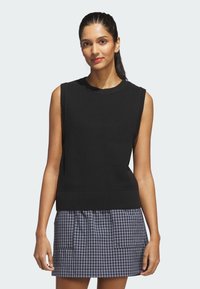 Czarny bezrękawnik z dzianiny z teksturowanym wzorem, prążkowanym dekoltem i dołem, zestawiony z kraciastą, krótką spódnicą z kieszeniami.