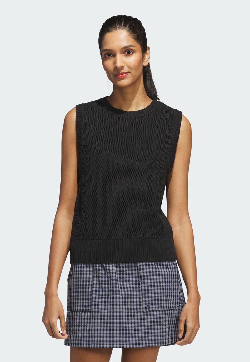 Czarny bezrękawnik z dzianiny z teksturowanym wzorem, prążkowanym dekoltem i dołem, zestawiony z kraciastą, krótką spódnicą z kieszeniami.