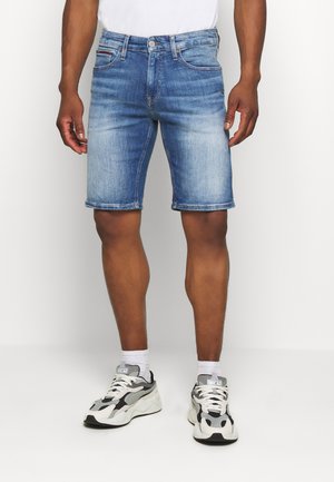 Jasnoniebieskie szorty dżinsowe z efektem sprania, klasycznym, pięciokieszeniowym krojem, prostą linią i podwiniętymi nogawkami, zestawione z masywnymi sneakersami.