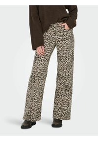 Hlače s leopard uzorkom u opuštenom kroju, s bež osnovom i tamnosmešnim i crnim mrljama, napravljene od mekog materijala i uparene s crnim čizmama.