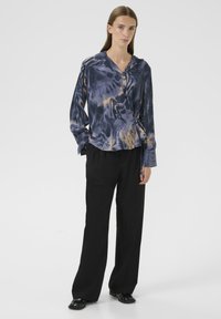 Zijden blouse met een blauw en geel abstract patroon, met een wikkeldesign en lange mouwen, gecombineerd met losse zwarte broek.