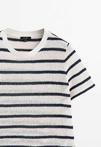 Dzianinowa koszulka z krótkim rękawem o poziomych paskach w kolorze granatowym i białym. Posiada prążkowany, okrągły dekolt oraz luźny krój.