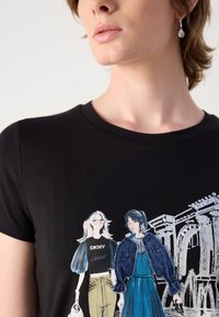 Black cotton t-shirt featuring a graphic print of two illustrated figures wearing DKNY apparel with varying styles. Round neckline, short sleeves.