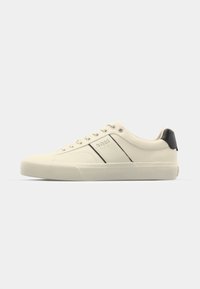 Cream-colored sneakers with a smooth texture, featuring black accents and branding. Classic lace-up design with a round toe and rubber sole.