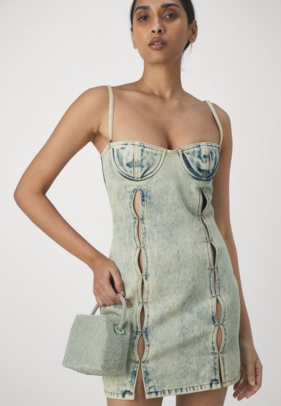 Denim minikjole med lys blå vask, hjerteformet utringning, utskjæringer på sidene og tynne stropper. Håndholdt glitrende grønn veske.