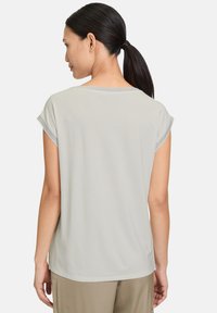 Haut gris clair à manches courtes avec un col rond et un contour gris contrastant aux manches. Tissu lisse avec une coupe décontractée.