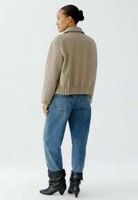 Graue Wollmischungjacke mit Kragen und elastischem Saum, kombiniert mit hellblauen Jeans und schwarzen lässigen Knöchelstiefeln.