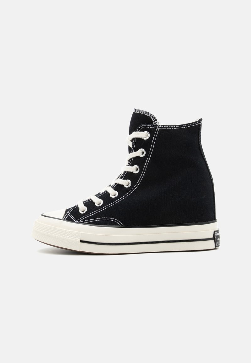 Svarte høye sneakers laget av lerret, med hvite sømmer, snøring foran, gummitåhette og teksturert hvit såle.