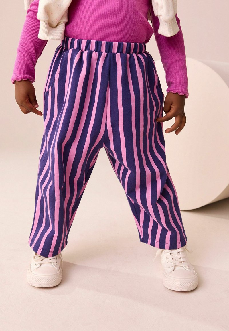 Un pantalon rayé en coton violet et rose, doté d'une taille élastique et de deux poches latérales, associé à des baskets blanches.