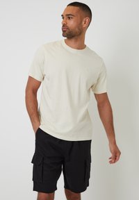 Camiseta de manga corta color crema hecha de tela suave, combinada con pantalones cortos cargo negros con bolsillos laterales y un ajuste relajado.