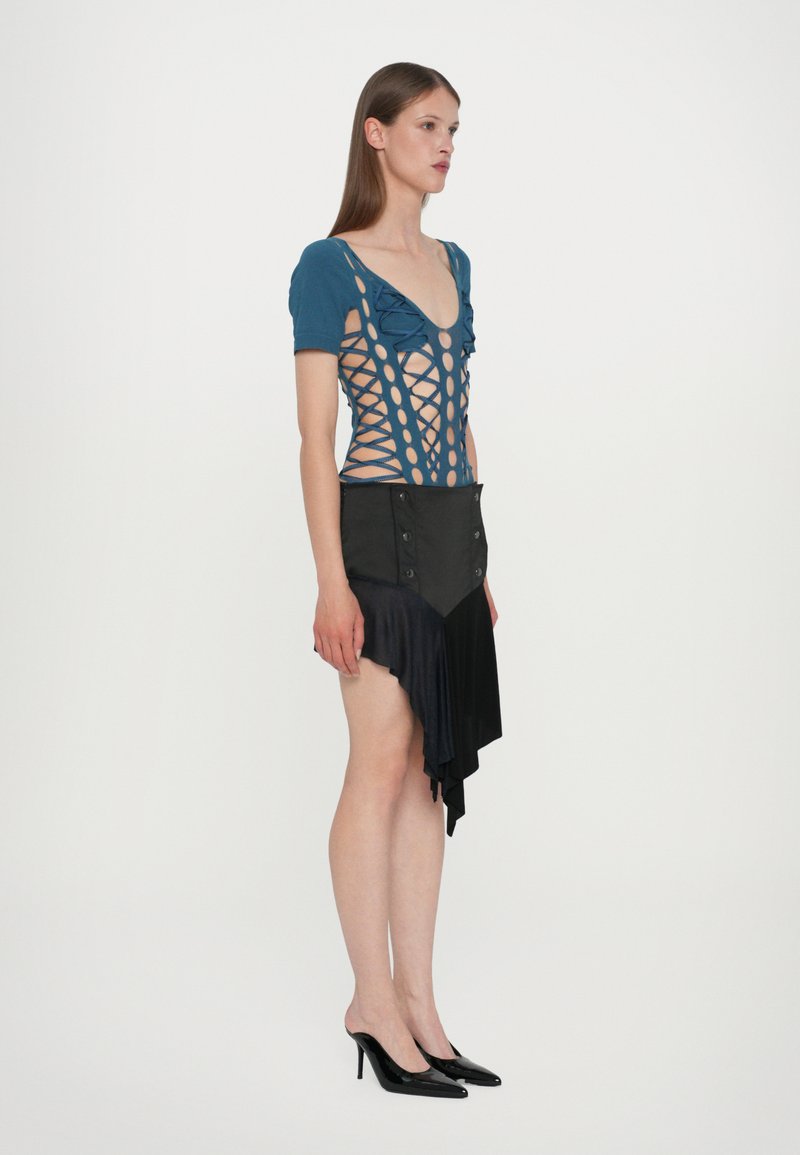 Teal bodysuit with cutouts and ruffled sleeves, paired with a black asymmetrical skirt featuring button details and a smooth texture.