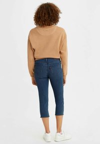 Bruine sweatshirt met een ronde hals; gecombineerd met verkorte blauwe denim jeans; witte sneakers. Casual outfit met gestructureerde materialen en contrasterende kleuren.