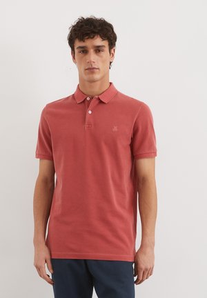 Polo rouge en coton doux, avec un col classique, des manches courtes et un petit logo sur la poitrine. Porté avec un pantalon navy.