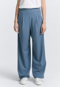 Lichtblauwe wijde broek met plooien, een hoge elastische tailleband en een soepele textuur, gecombineerd met witte sneakers.
