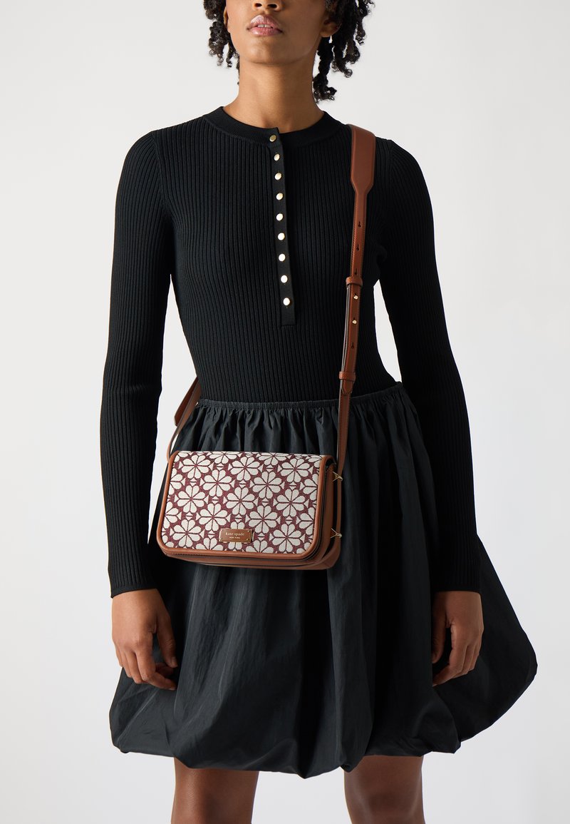 Borsa a spalla marrone con motivo floreale in bordeaux e bianco, dotata di chiusura a patta e hardware dorato, indossata con un vestito nero a coste.