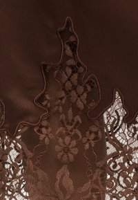 Σκούρο καφέ ύφασμα με κυματιστή άκρη που καλύπτει δαντέλα με λουλουδένιο σχέδιο σε παρόμοιες καφέ αποχρώσεις.