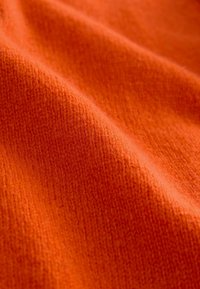 Orange gestrickter Stoff mit einer weichen, strukturierten Oberfläche. Das Material weist ein feines, gleichmäßiges Gewebe und subtile Farbtonvariationen auf.