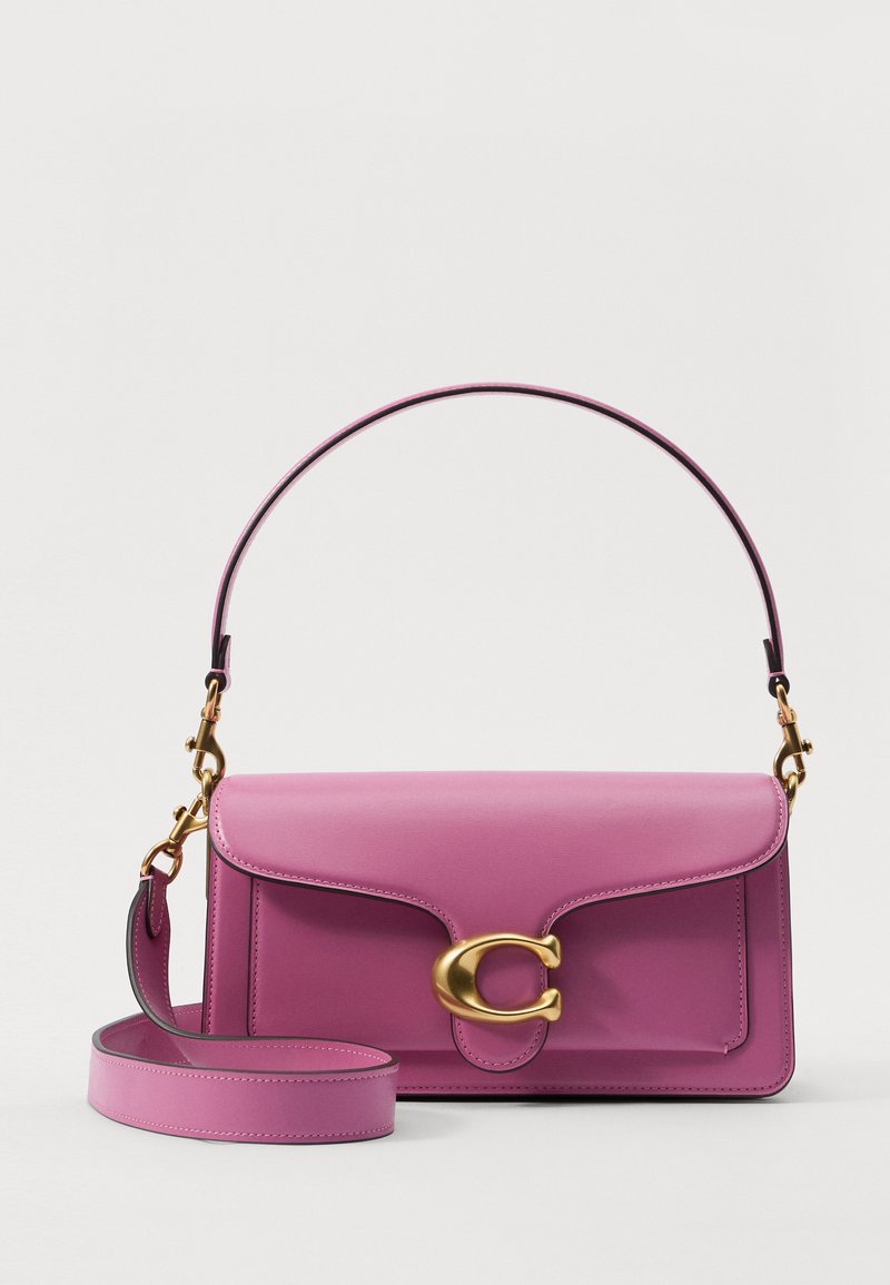 Violeta ādas soma ar zeltaini spiedētu aizdari, plakana forma un noņemama plecu siksna. Īpašības: gluda tekstūra un minimāls dizains.