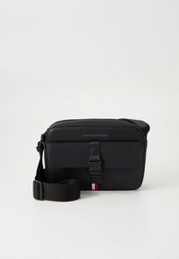 Musta õlakott siledast tekstuurist, reguleeritava sangaga, pandlaga kinnitusega ning allosas punane-valge-sinine triip.