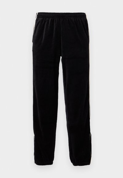 Pantalons de survêtement en velours noir avec une taille élastique, des poches latérales et des rayures blanches le long des coutures. Design à jambe fuselée.