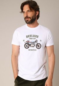 T-shirt en coton blanc avec un graphique de moto et le texte "DEELUXE ROAD CLUB 1974 MOTORCYCLES" en couleurs vertes et brunes.