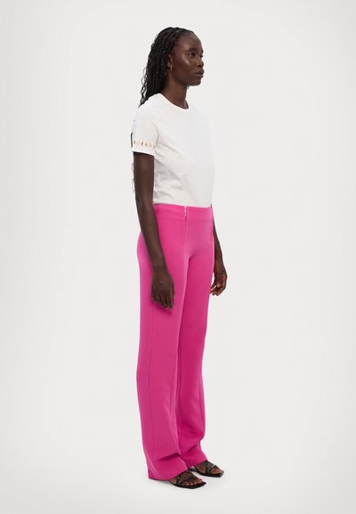 T-shirt blanc à manches courtes avec des accents de rayures colorées sur les manches, associé à un pantalon large rose vif ajusté. Fini en tissu lisse.