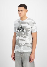 Γκρίζα μπλούζα κοντομάνικη με παραλλαγή, στρογγυλή λαιμόκοψη και λογότυπο "Alpha Industries" σε μαύρο χρώμα. Μαλακό βαμβακερό υλικό με ομαλή υφή.