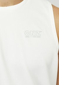 Bijela majica bez rukava za sport, izrađena od teksturiranog materijala. Ima mali, nejasan logo "CNZ" na grudima.