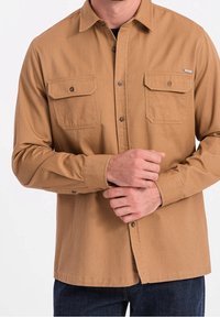 Brązowa koszula zapinana na guziki, wykonana z bawełny, z dwoma kieszeniami na piersi, klasycznym kołnierzykiem, długimi rękawami i prostym dołem.