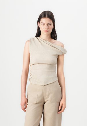 Beige Trägershirt aus strukturiertem Stoff mit gerafften Details und asymmetrischem Saum, kombiniert mit beigen weiten Hosen.