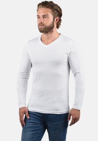 Fehér, hosszú ujjú, V-nyakú, testre szabott ing, sima, könnyű anyagból készült, kék farmerrel párosítva.